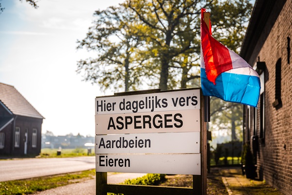 Schild mit regionalen Limburger Produkten wie Spargel, die dort unter einer holländischen Flagge verkauft werden