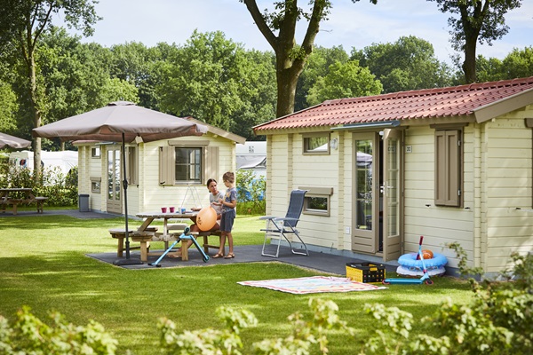 Die Familie genießt einen Sommertag im Ferienpark de Leistert in Leudal, mit Holzchalets und einem Picknicktisch im Gras.