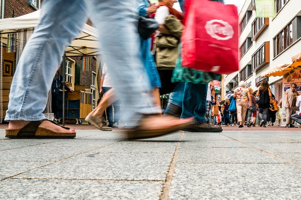 Busy shopping street during shopping Sunday in Weert. In the foreground, people walk by, focusing on their feet and bags. Shoppers, market stalls and shops can be seen in the background.