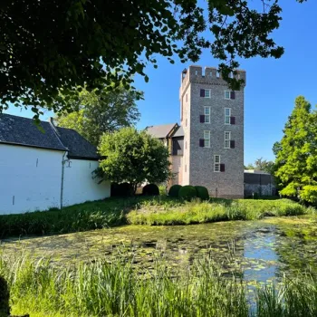 Kasteel Daelenbroeck in Herkenbosch, een historische toren omgeven door water en groen, stralend in de zon aan de rand van Nationaal Park De Meinweg.